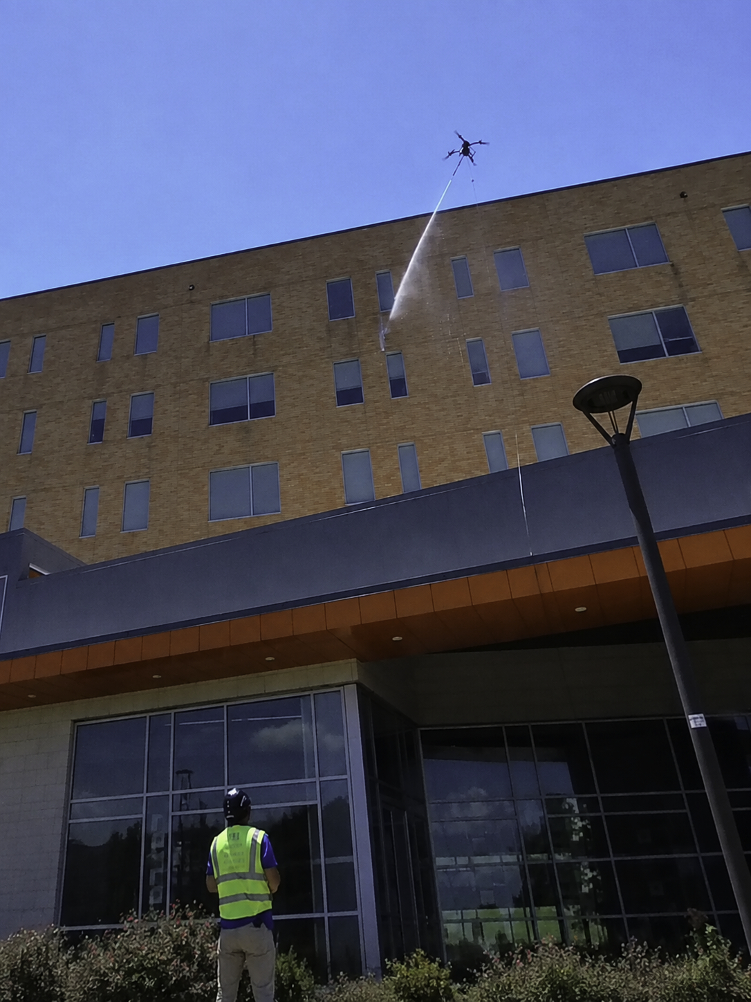 Helios Drone Washing FAA Part 107-certified pilot operating a spray drone to clean a multi-story commercial building.